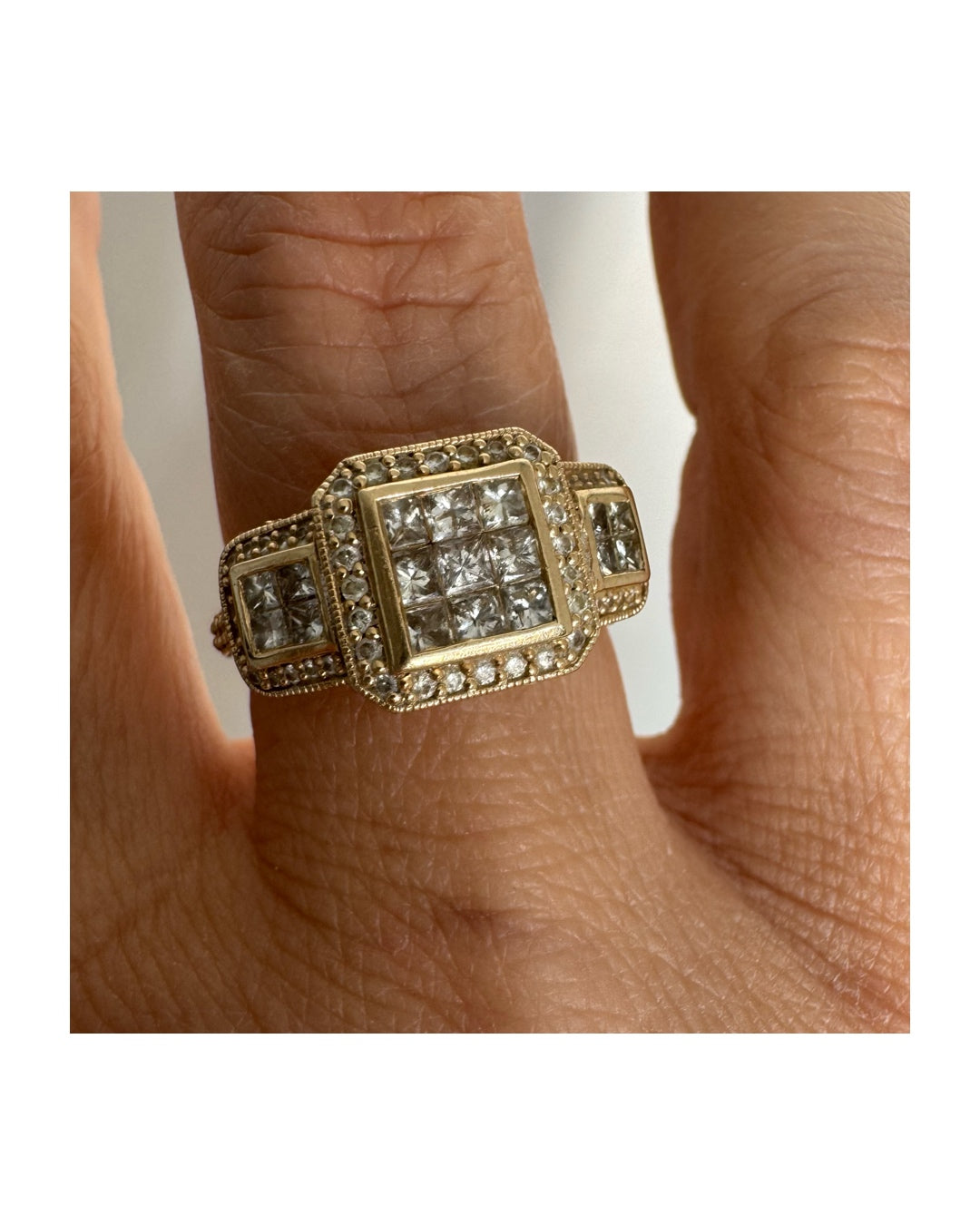 טבעת זהב צהוב 14 קראט משובצת יהלומים בחיתוך פרינסס במרכז, מוקפת הילה של יהלומים צדדיים.