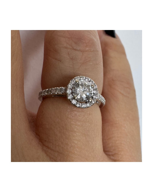 טבעת זהב לבן 14 קראט משובצת יהלום מרכזי עגול והילה נוצצת של יהלומים קטנים, עם יהלומים נוספים על החישוק.