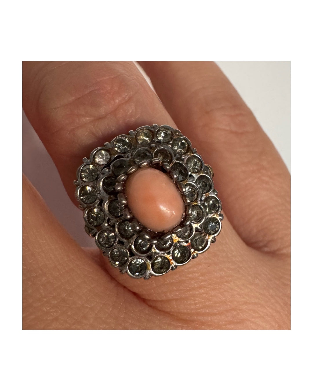 טבעת וינטג׳ עם חלק תחתון מזהב 14 קראט וחלק עליון עשוי כסף משובצת אבן קורל בהירה במרכז ומסביבה אבנים בהירות שאינן יהלומים.