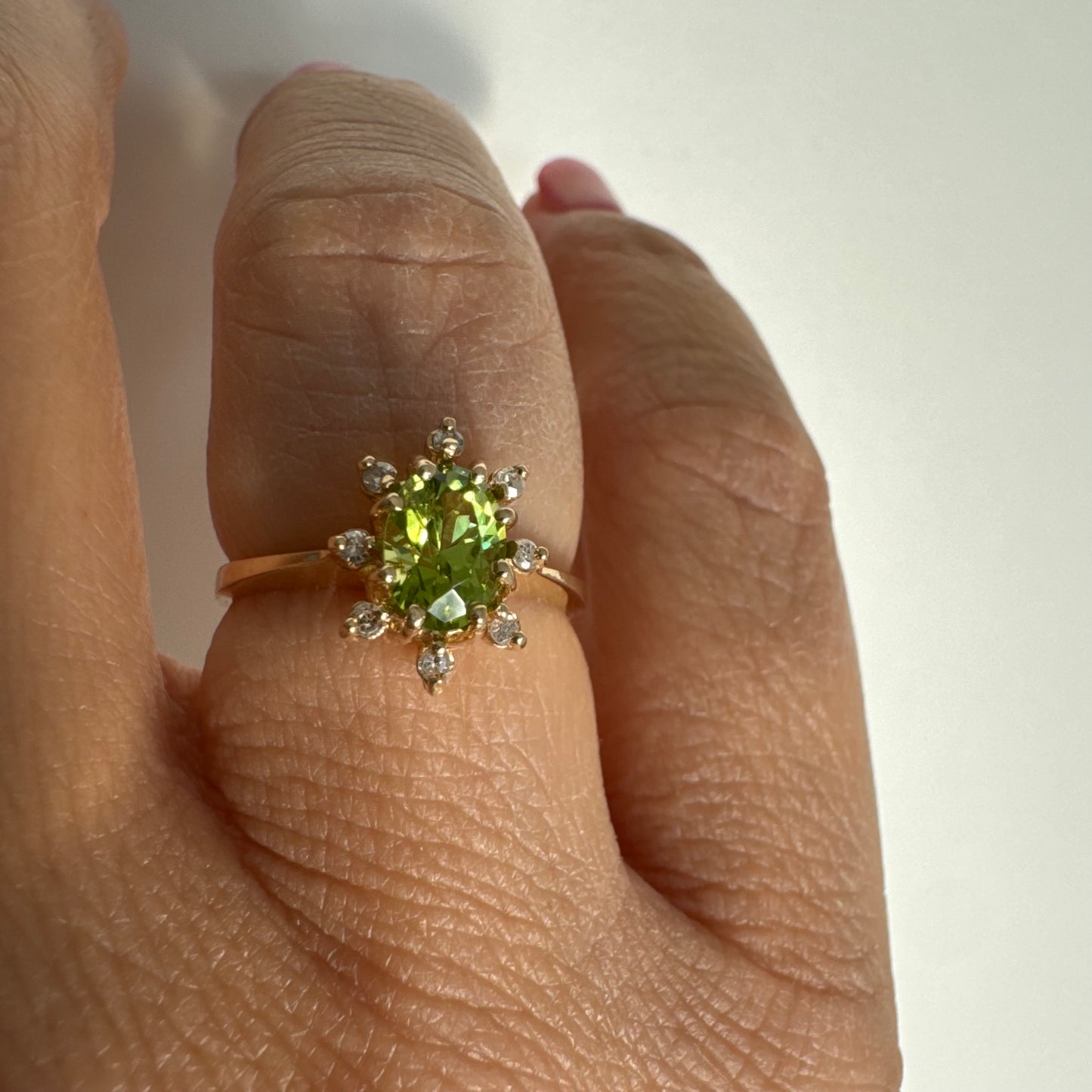 טבעת זהב 14 קראט משובצת אבן פרידוט ירוקה בחיתוך אובלי, מוקפת יהלומים היוצרים הילה עדינה מסביבה.