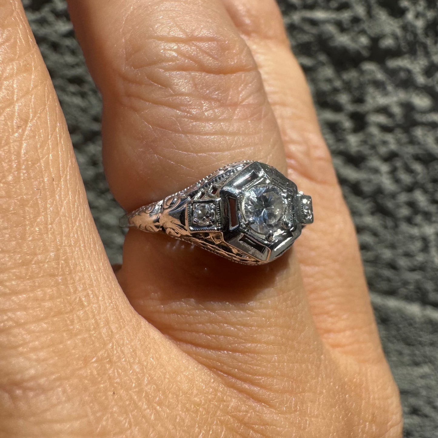 14K gold ring set with a central round diamond, framed by geometric Art Deco details and additional accent stones.