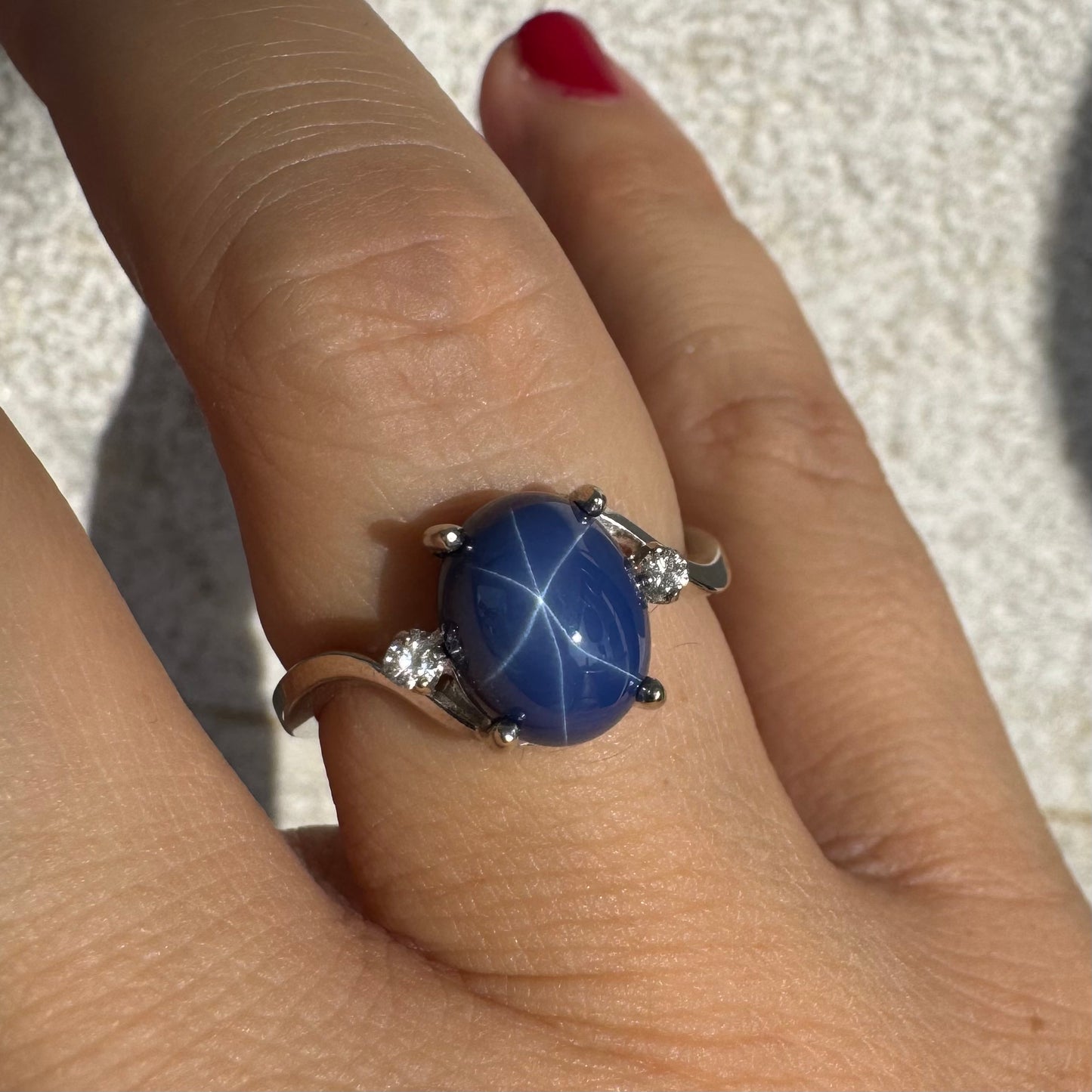 טבעת זהב לבן 14 קראט משובצת אבן ספיר כוכב מרהיבה, המציגה תופעת טבע של שישה קווים זוהרים, ובצידיה שני יהלומים מנצנצים. 