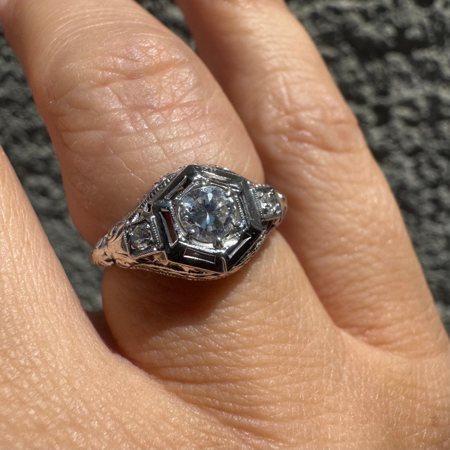 14K gold ring set with a central round diamond, framed by geometric Art Deco details and additional accent stones.