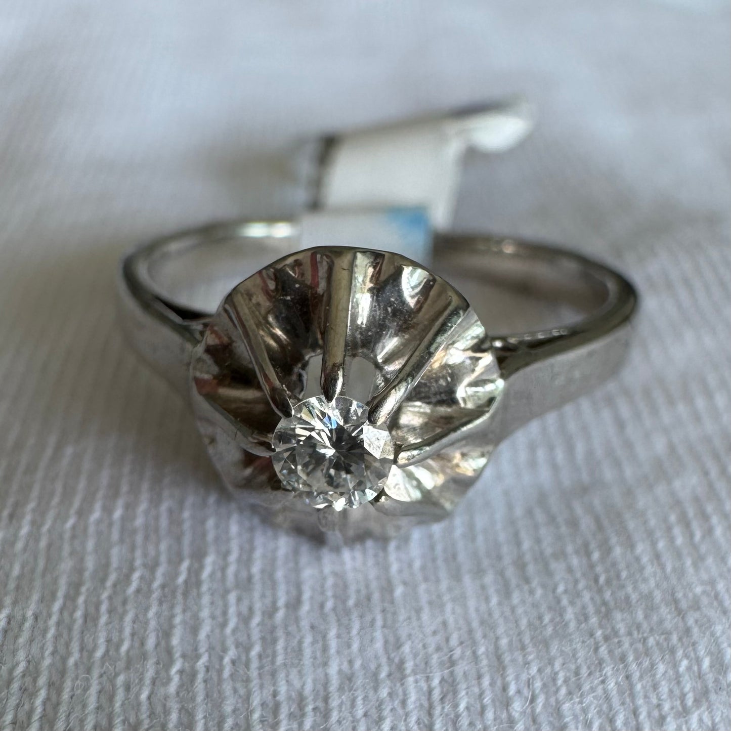 טבעת זהב לבן 18 קראט בעיצוב פיסולי עם יהלום מרכזי בחיתוך מבריק, משובץ במסגרת מחורצת שמשקפת את האור בעוצמה