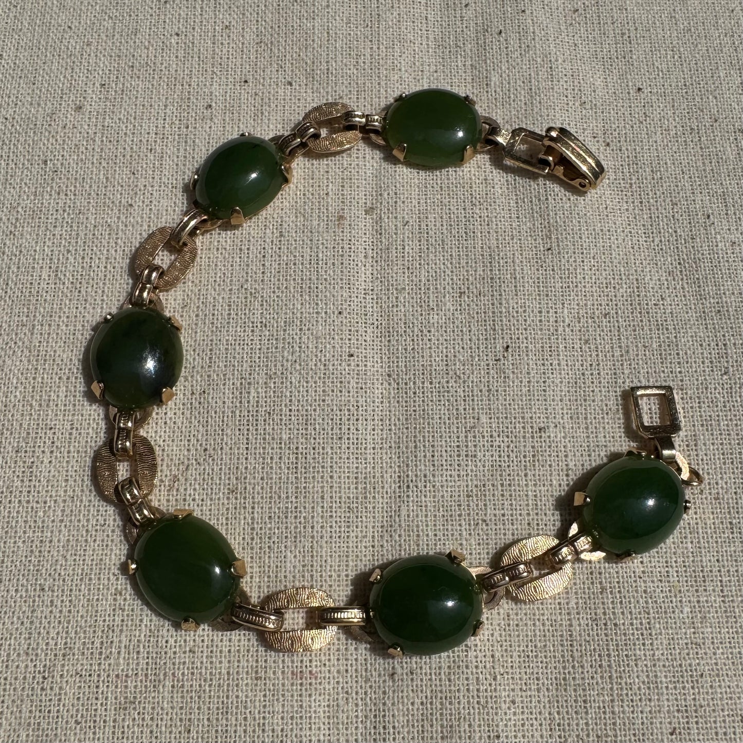 צמיד זהב צהוב 14 קראט משובץ באבני ג’ייד ירוקות בחיתוך קבושון (cabochon) בעיצוב אליפטי, המחוברות ביניהן בחוליות זהב עם טקסטורה מעניינת.