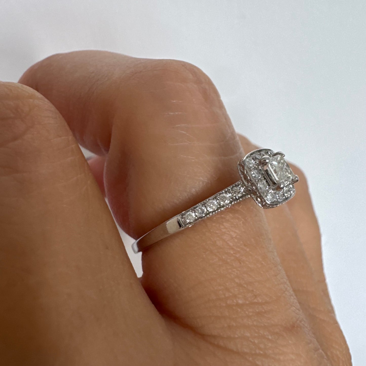 טבעת זהב לבן 14 קראט משובצת יהלום מרכזי בחיתוך פרינסס, מוקף הילת יהלומים קטנים וזרוע משובצת פאווה