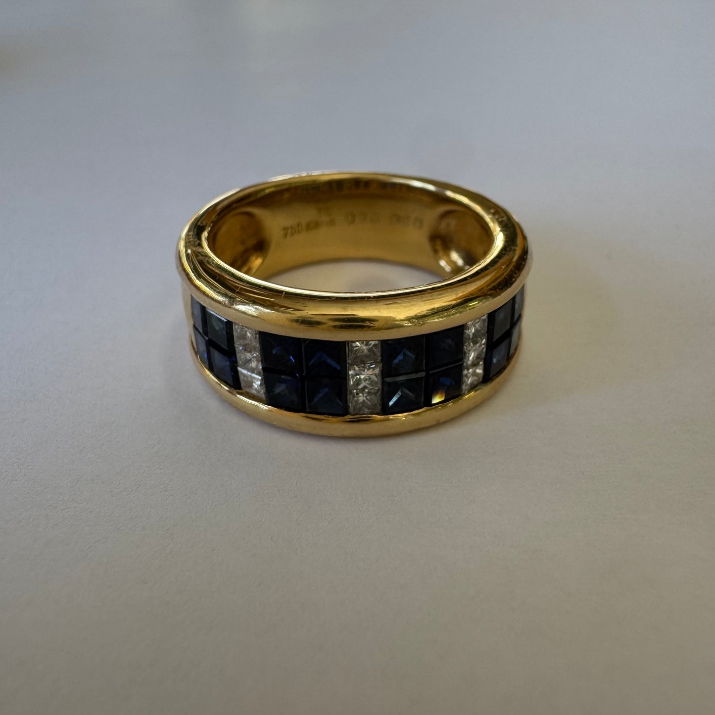 טבעת ה.שטרן זהב צהוב 18 קראט, בעיצוב רחב ומרשים. משובצת שורת אבני ספיר כחולות מרובעות בשילוב מחיצות של יהלומים לנגיעת ברק יוקרתי.