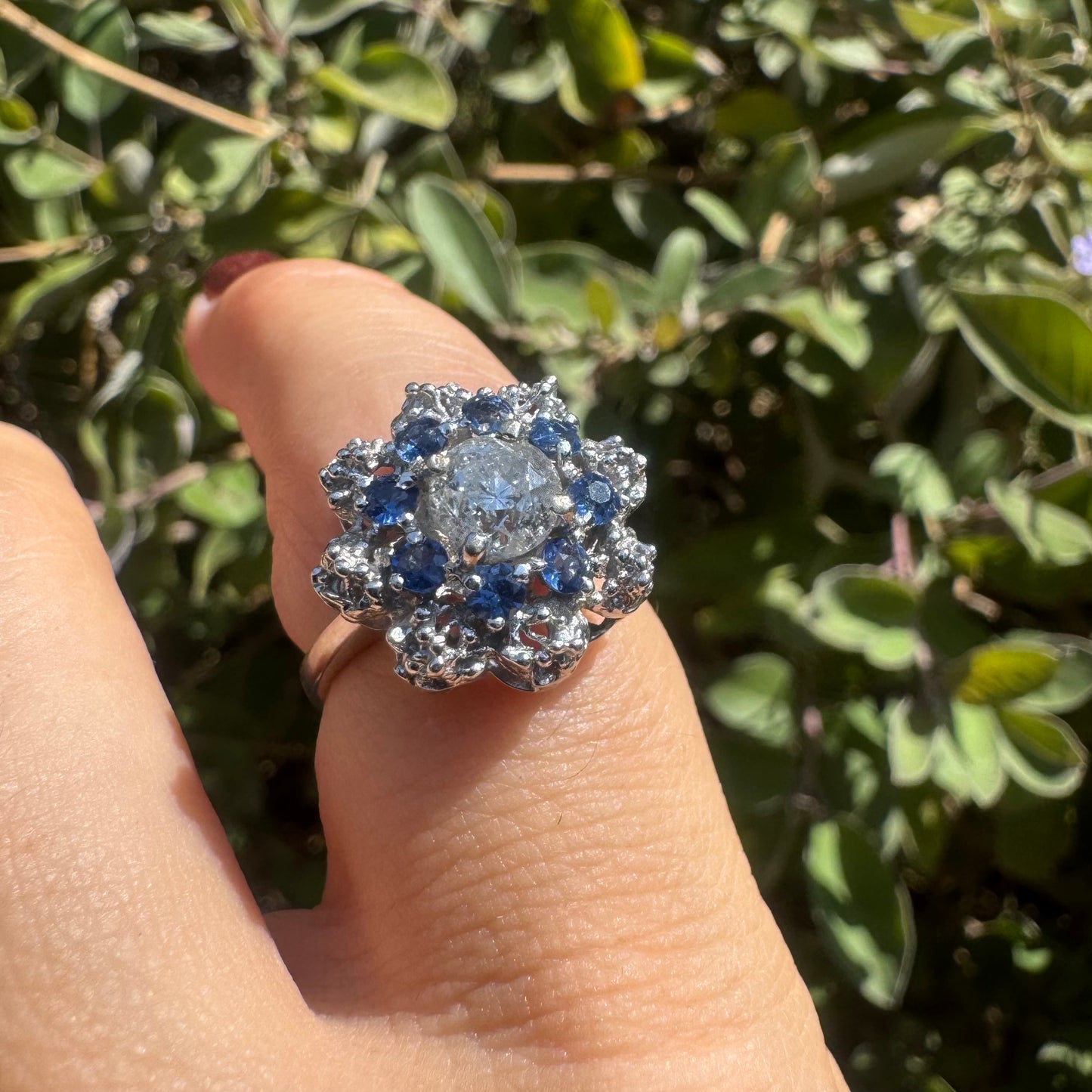 18K gold ring featuring a large round Diamond at the center, surrounded by a floral halo of purple -blue Tanzanite and & Diamonds.