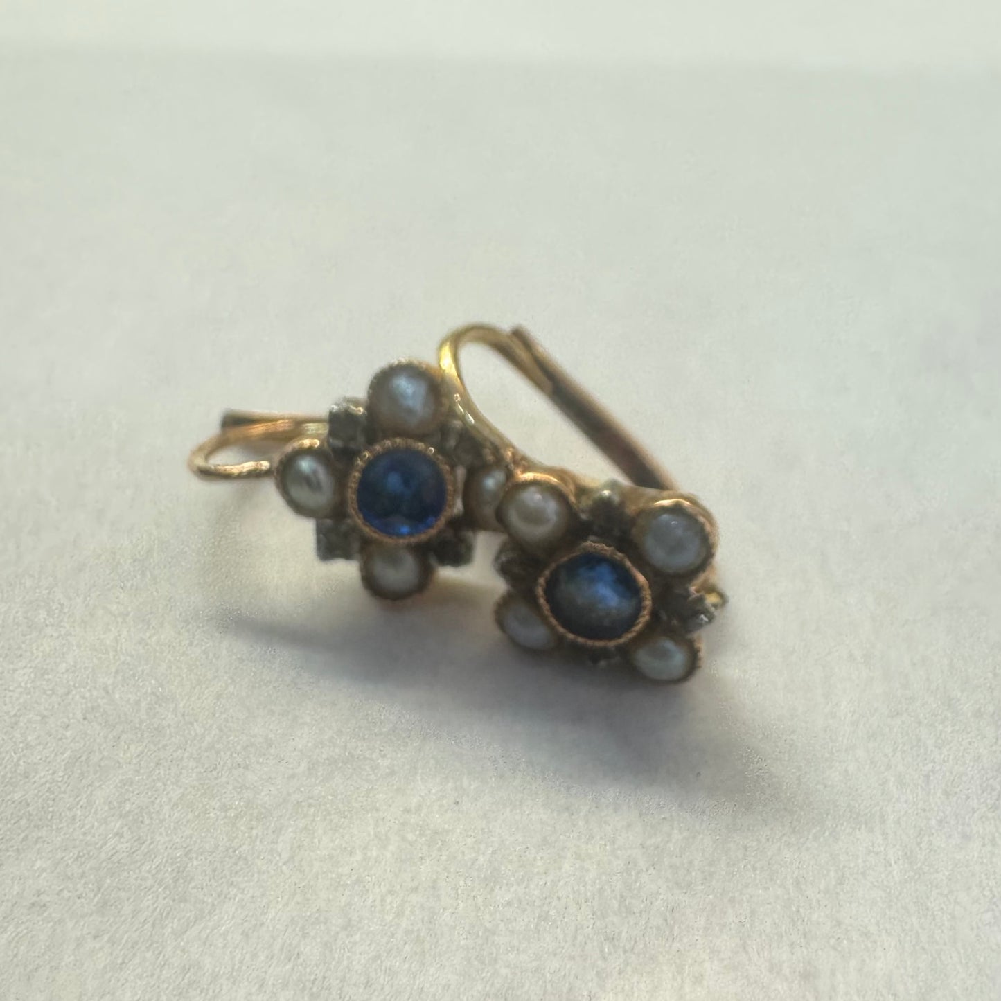 עגילי זהב 14 קראט משובצים אבן ספיר במרכז וסביבה משובצות פנינים קטנות בעיצוב פרחוני