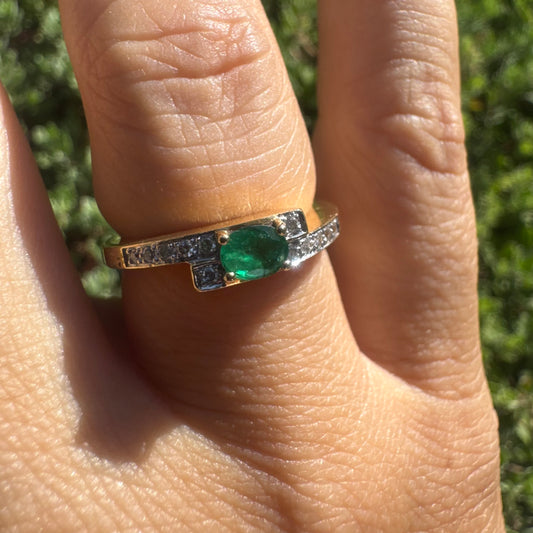 18K gold ring set with an oval green Emerald at the center, accented with sparkling Diamonds along the band.