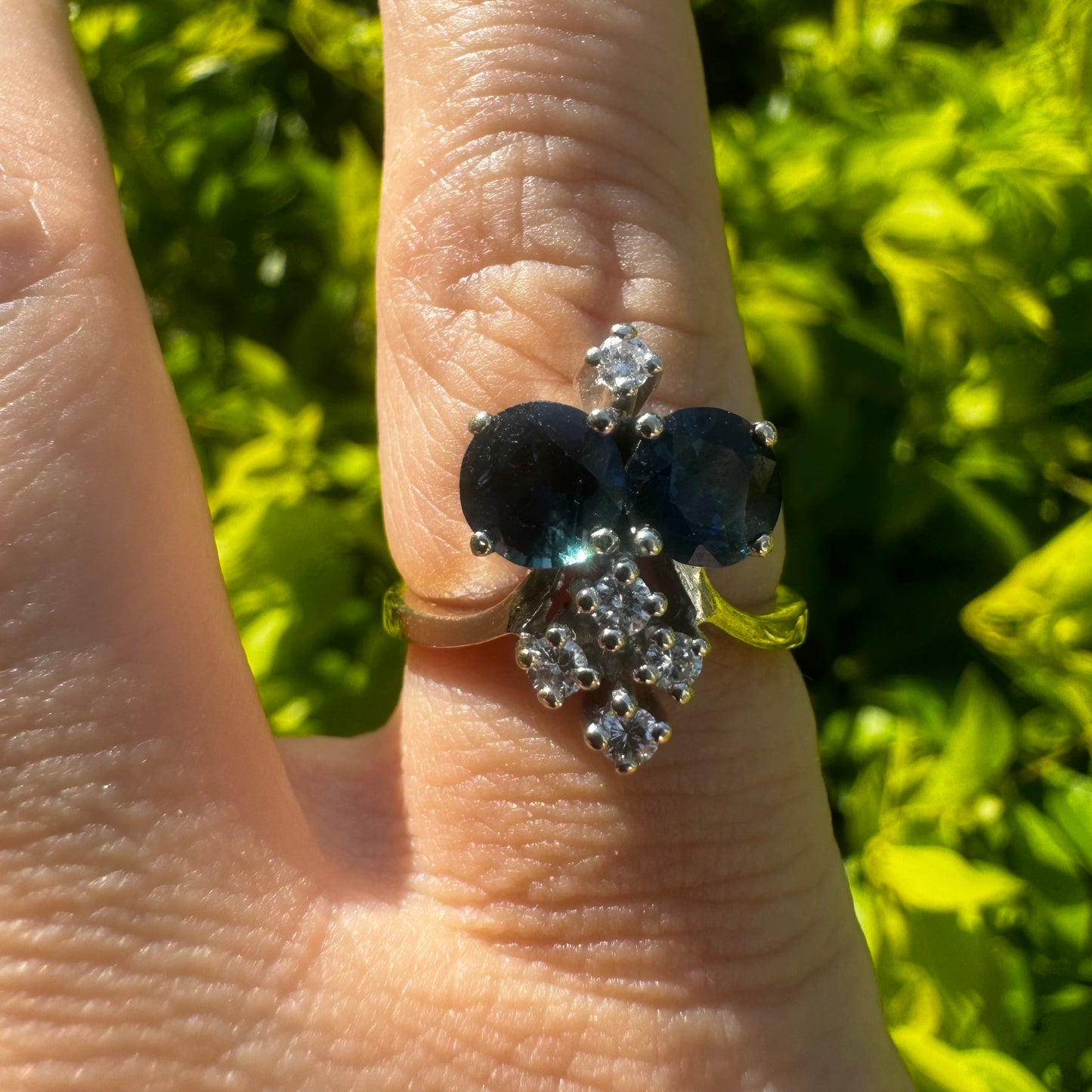 14K gold ring set with two deep blue oval Sapphires accented by clusters of brilliant white Diamonds.