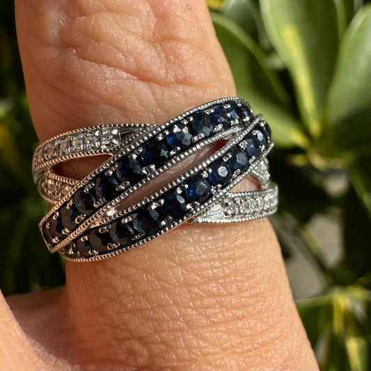 טבעת זהב לבן 14 קראט,קרוס, בעיצוב אלגנטי, משובצת בשורות של ספירים כחולים עמוקים ויהלומים מנצנצים.