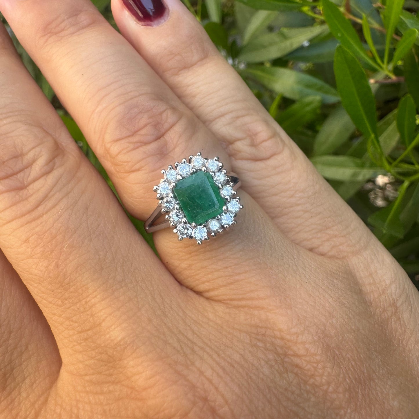 18K gold ring set with a green Emerald at the center, surrounded by a halo of sparkling round Diamonds.
