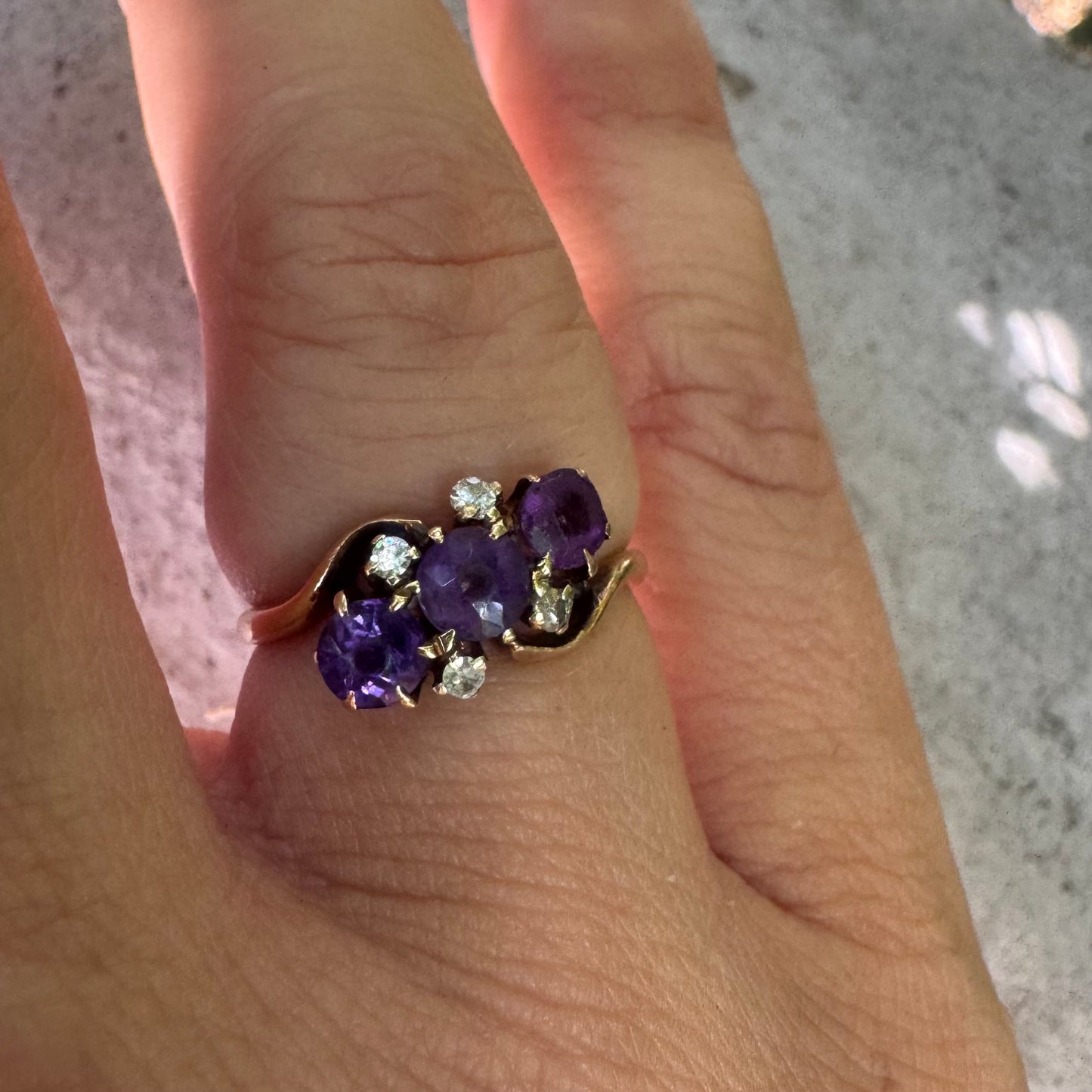 14K gold ring set with three round purple amethysts, accented by small sparkling Diamonds.