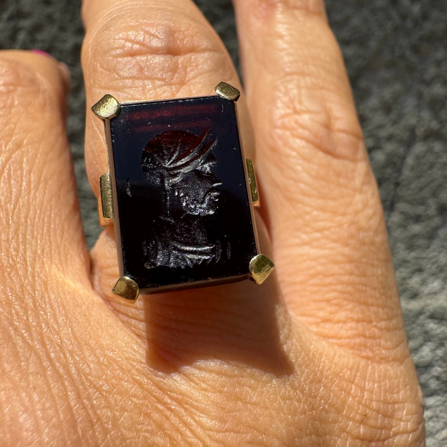 18K gold ring set with a carved dark stone featuring a classical warrior profile.