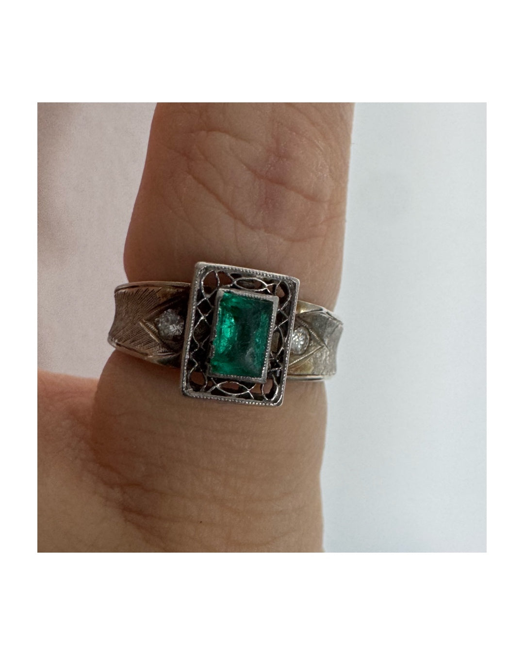 טבעת זהב לבן 14 קראט משובצת אבן אמרלד בחיתוך מלבני (Emerald cut) במרכז, מוקפת במסגרת מלבנית עם עבודת פיליגרן עדינה.