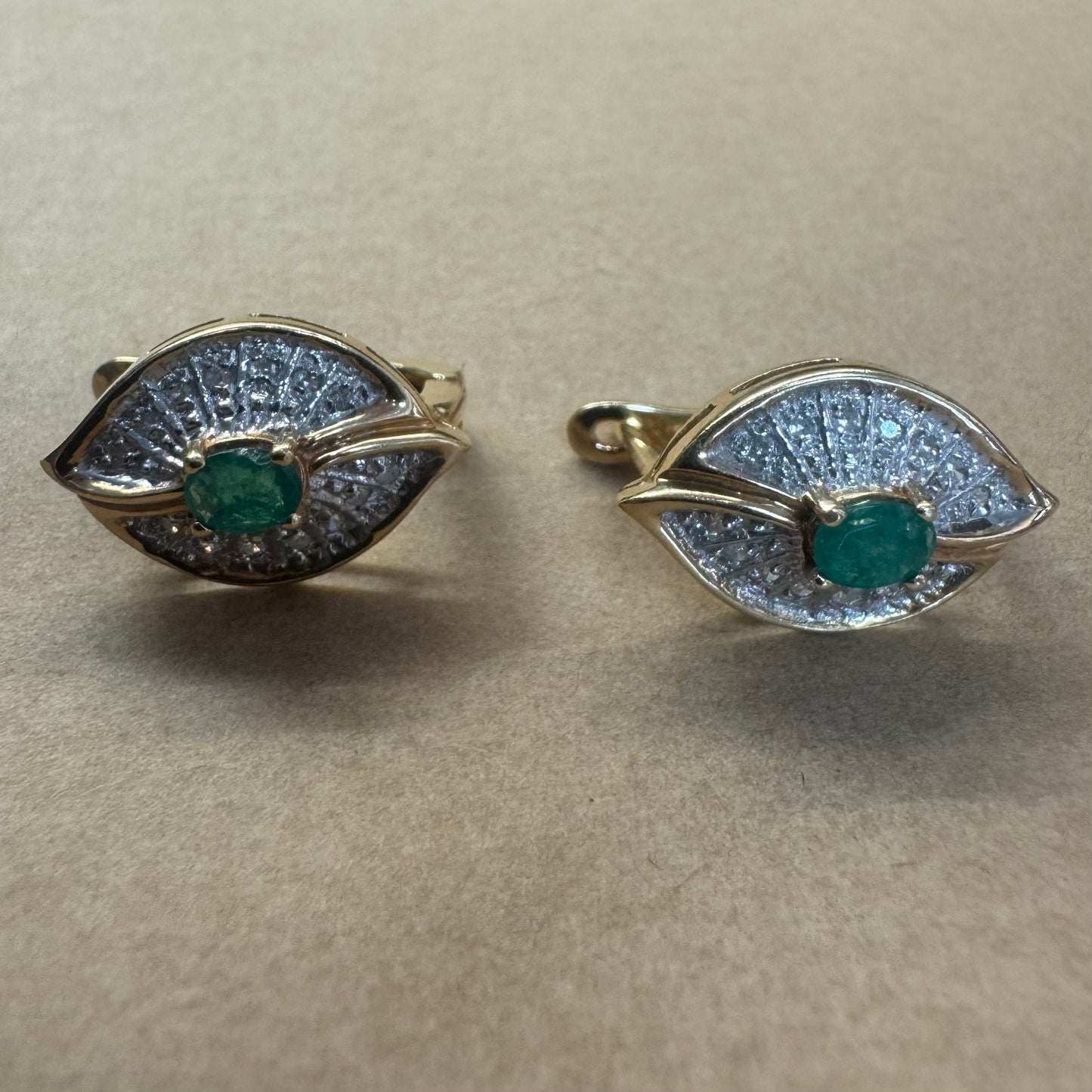 עגילים צמודים לאוזן, זהב צהוב 14 קראט, משובצים אמרלד במרכז, וסביבן פיתוחים משובצים יהלומים, שמעניקים מראה של ניצוץ רך ואלגנטי
