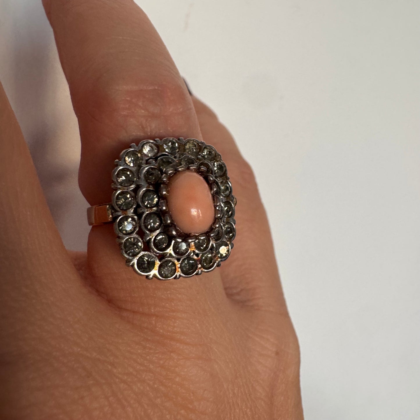 טבעת וינטג׳ עם חלק תחתון מזהב 14 קראט וחלק עליון עשוי כסף משובצת אבן קורל בהירה במרכז ומסביבה אבנים בהירות שאינן יהלומים.