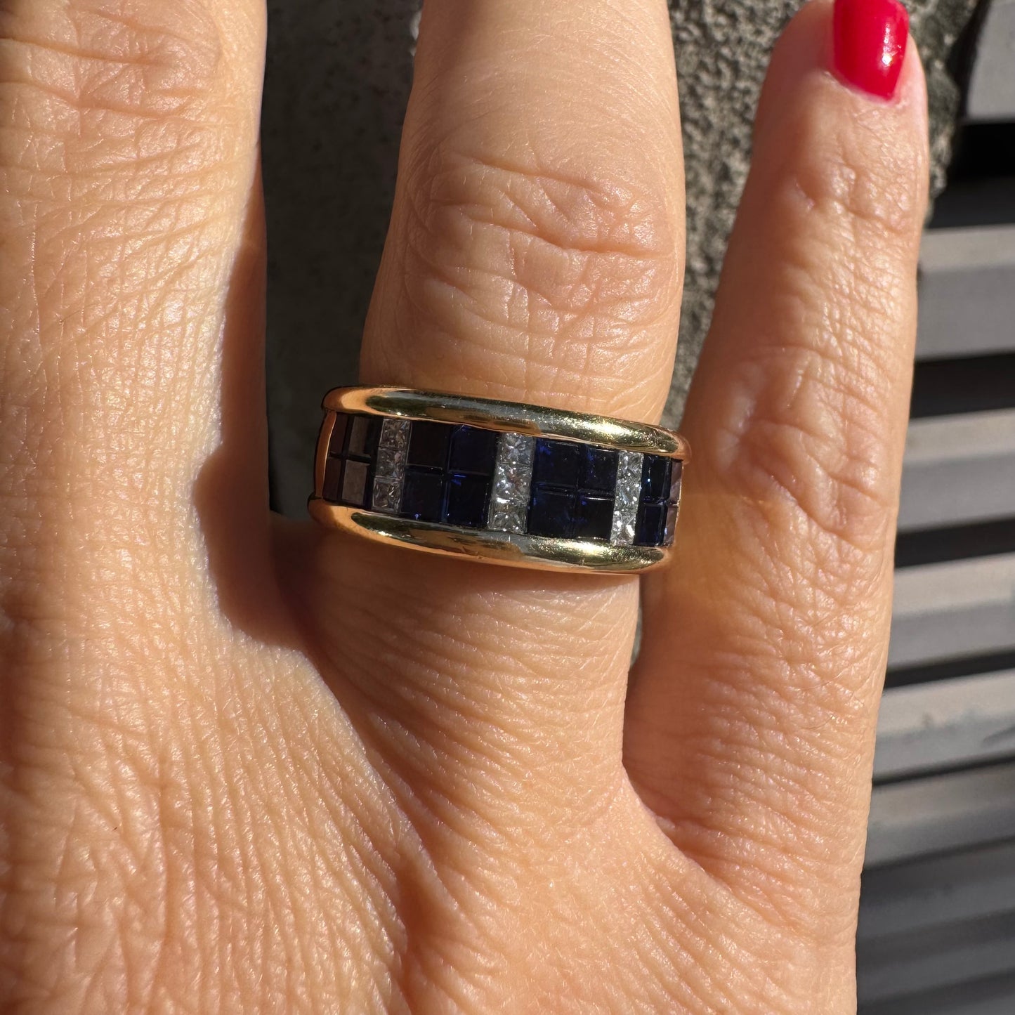 טבעת ה.שטרן זהב צהוב 18 קראט, בעיצוב רחב ומרשים. משובצת שורת אבני ספיר כחולות מרובעות בשילוב מחיצות של יהלומים לנגיעת ברק יוקרתי.