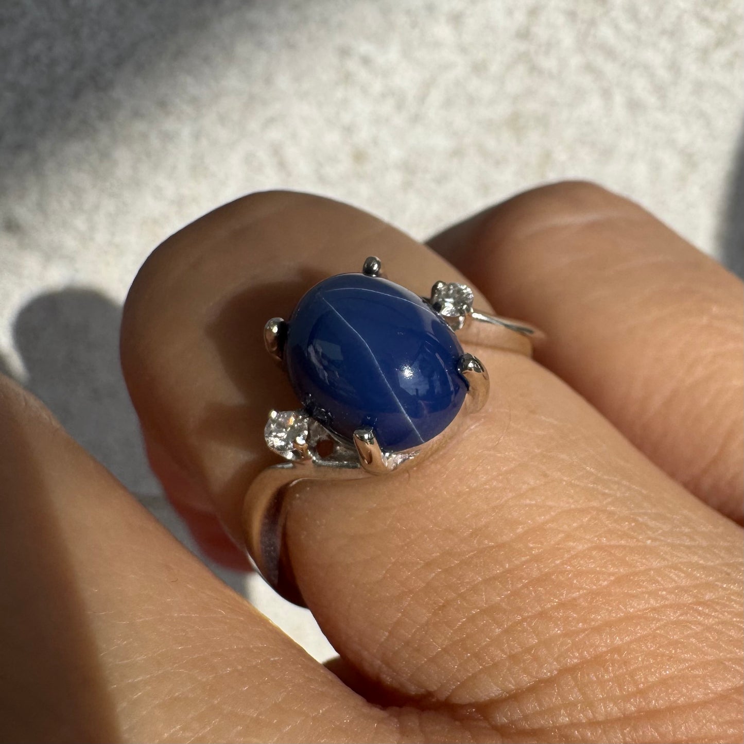 טבעת זהב לבן 14 קראט משובצת אבן ספיר כוכב מרהיבה, המציגה תופעת טבע של שישה קווים זוהרים, ובצידיה שני יהלומים מנצנצים. 