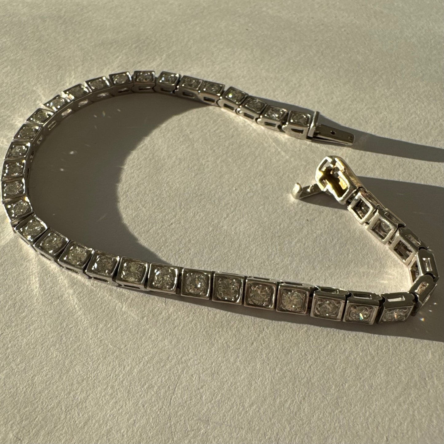 צמיד טניס זהב לבן 18 קראט משובץ יהלומים עגולים נוצצים בתוך מסגרות ריבועיות.