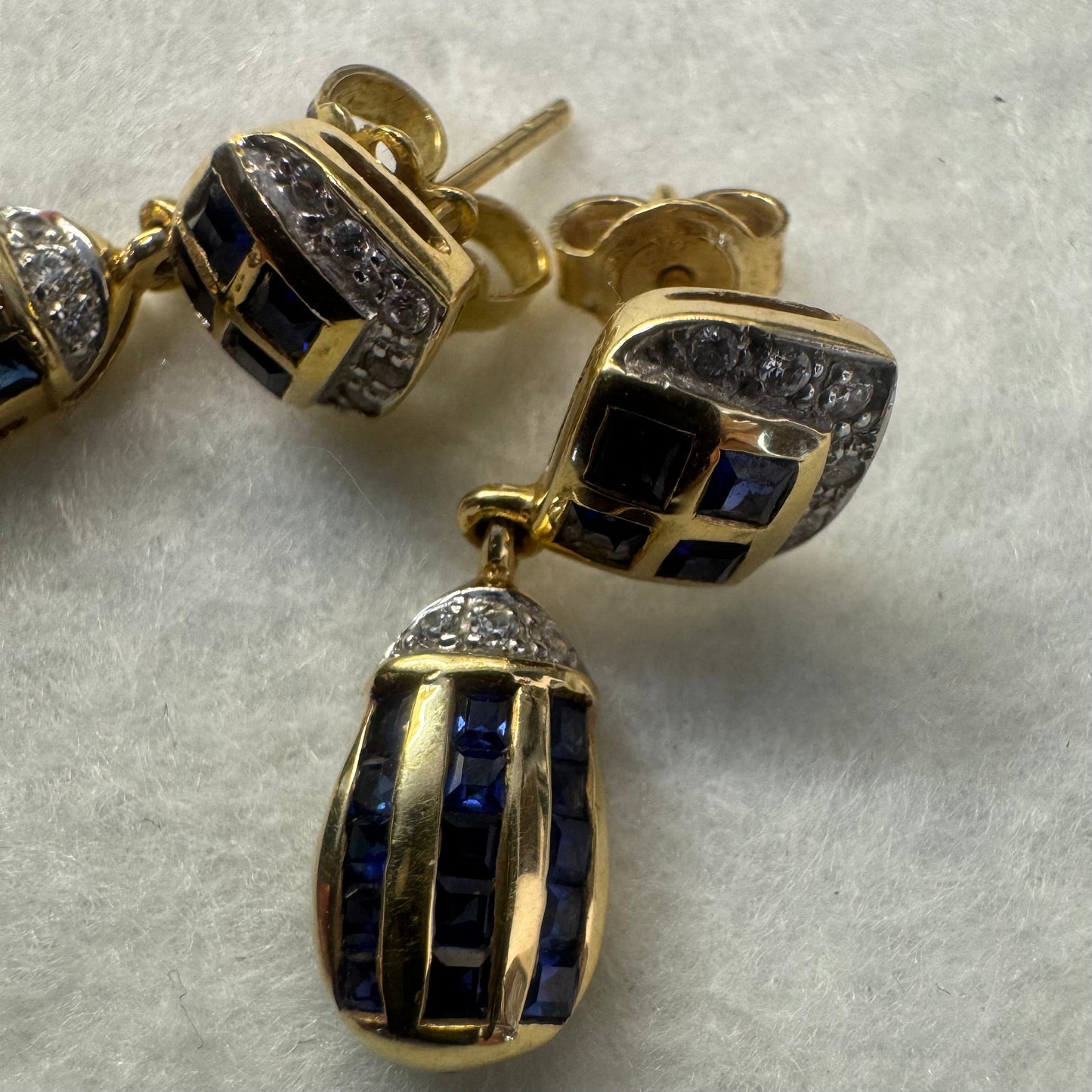 עגילי זהב צהוב 18 קראט תלויים, משובצים אבני ספיר כחולות בגוון כחול עמוק בעיצוב גיאומטרי, בשילוב יהלומים מנצנצים