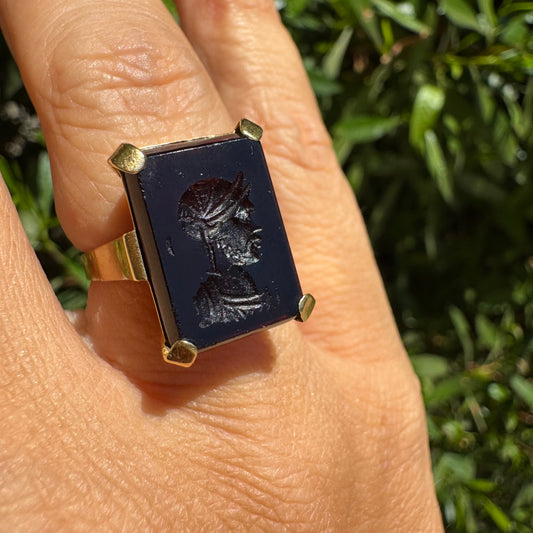 18K gold ring set with a carved dark stone featuring a classical warrior profile.