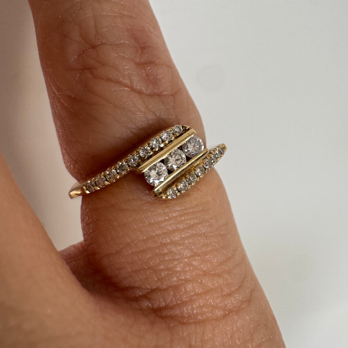 טבעת זהב צהוב 14 קראט בעיצוב ייחודי, משובצת שלושה יהלומים מרכזיים ושורות נוספות של יהלומים לאורך הזרועות. 