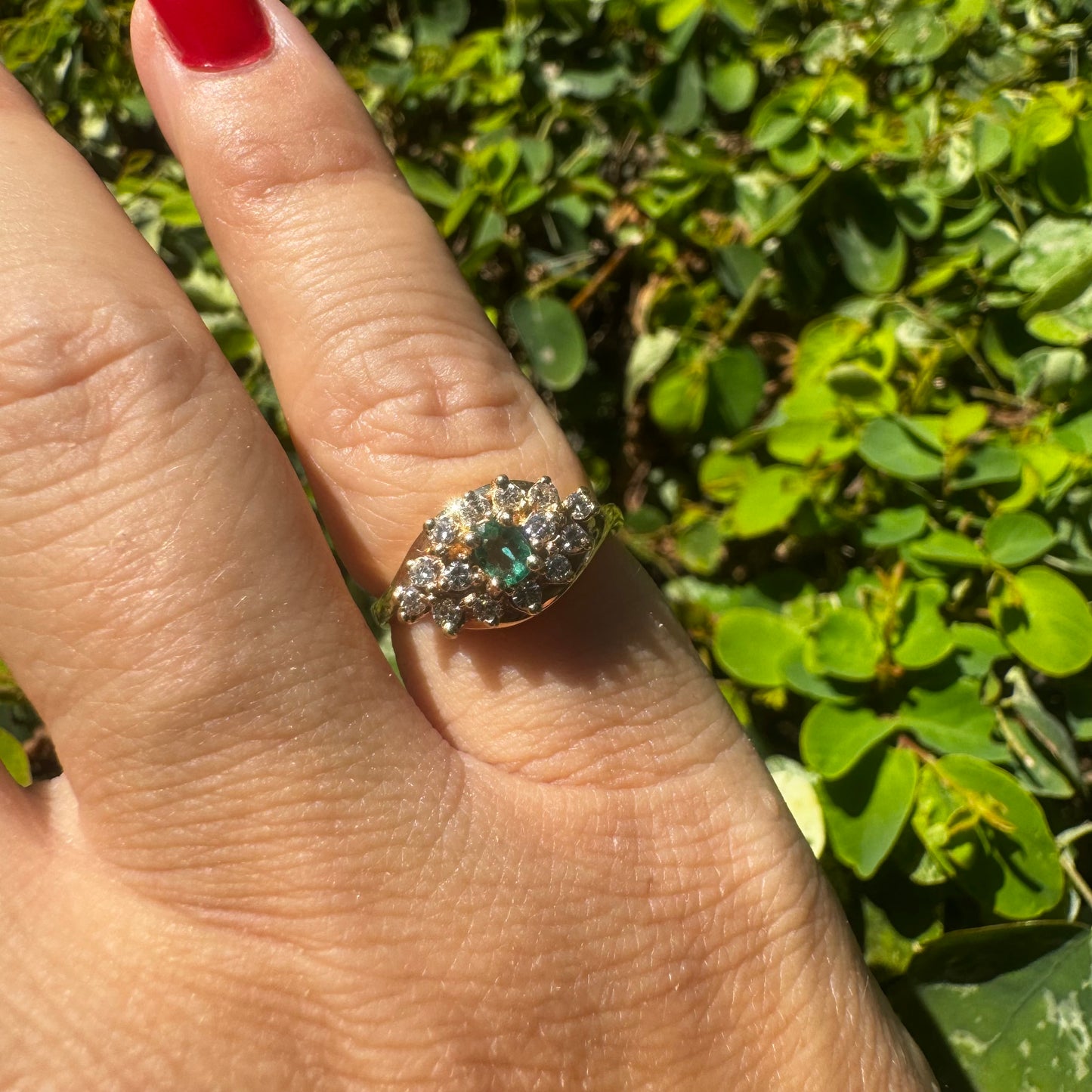 14K gold ring set with Emerald at its center, surrounded by a halo of brilliant-cut diamonds arranged in a floral-inspired cluster