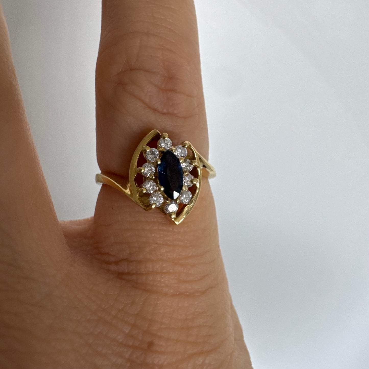 טבעת זהב צהוב 18 קראט משובצת ספיר כחול מרכזי בחיתוך מרקיזה, מוקף הילה של יהלומים המעניקים ניצוץ עדין ומדגישים את צבע האבן העמוק.