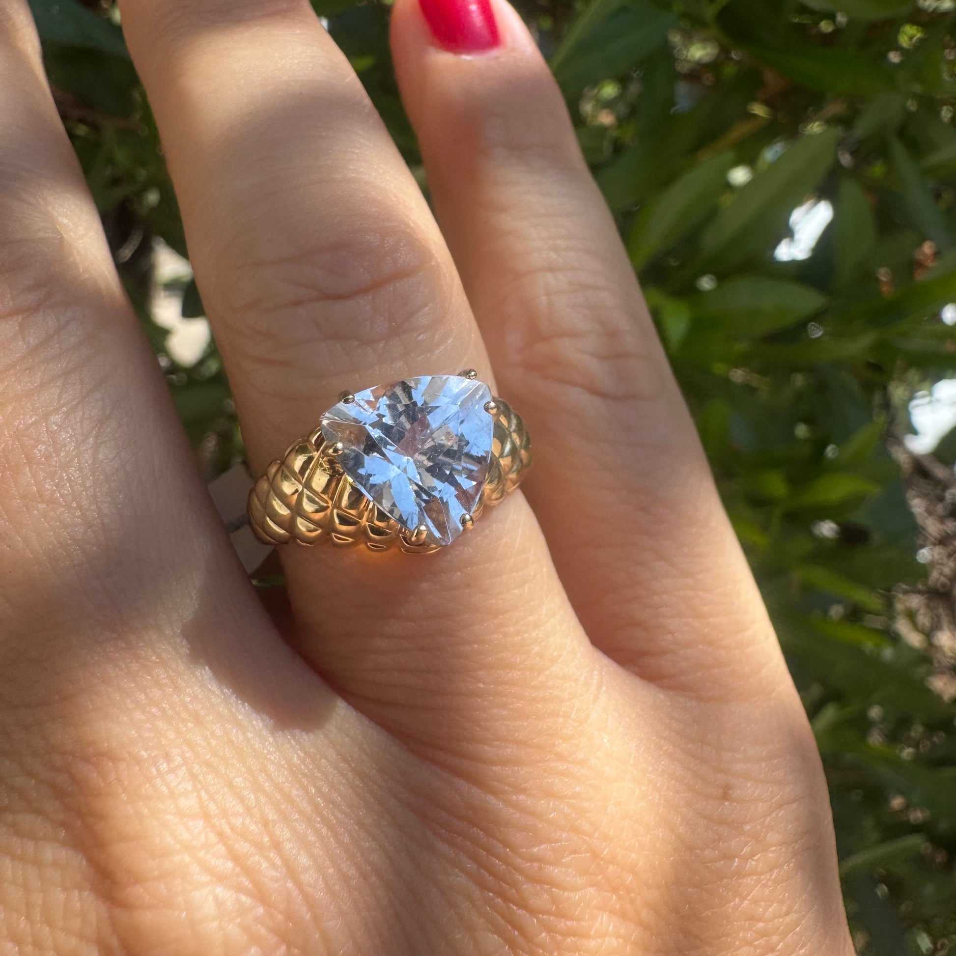 טבעת זהב צהוב 10 קראט משובצת אבן שקופה גדולה בחיתוך משולש, עם טבעת בעלת טקסטורה ייחודית ובולטת.