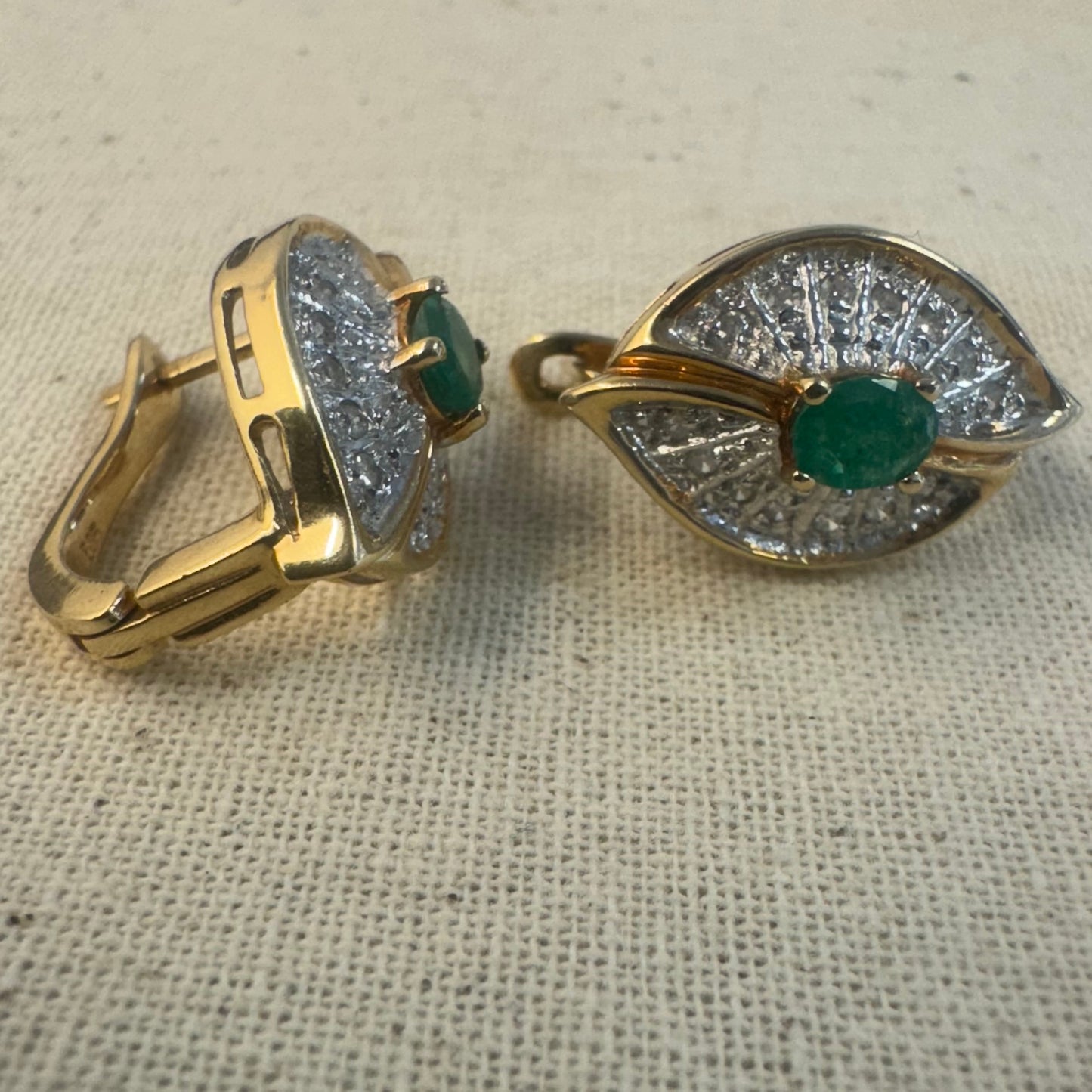 עגילים צמודים לאוזן, זהב צהוב 14 קראט, משובצים אמרלד במרכז, וסביבן פיתוחים משובצים יהלומים, שמעניקים מראה של ניצוץ רך ואלגנטי