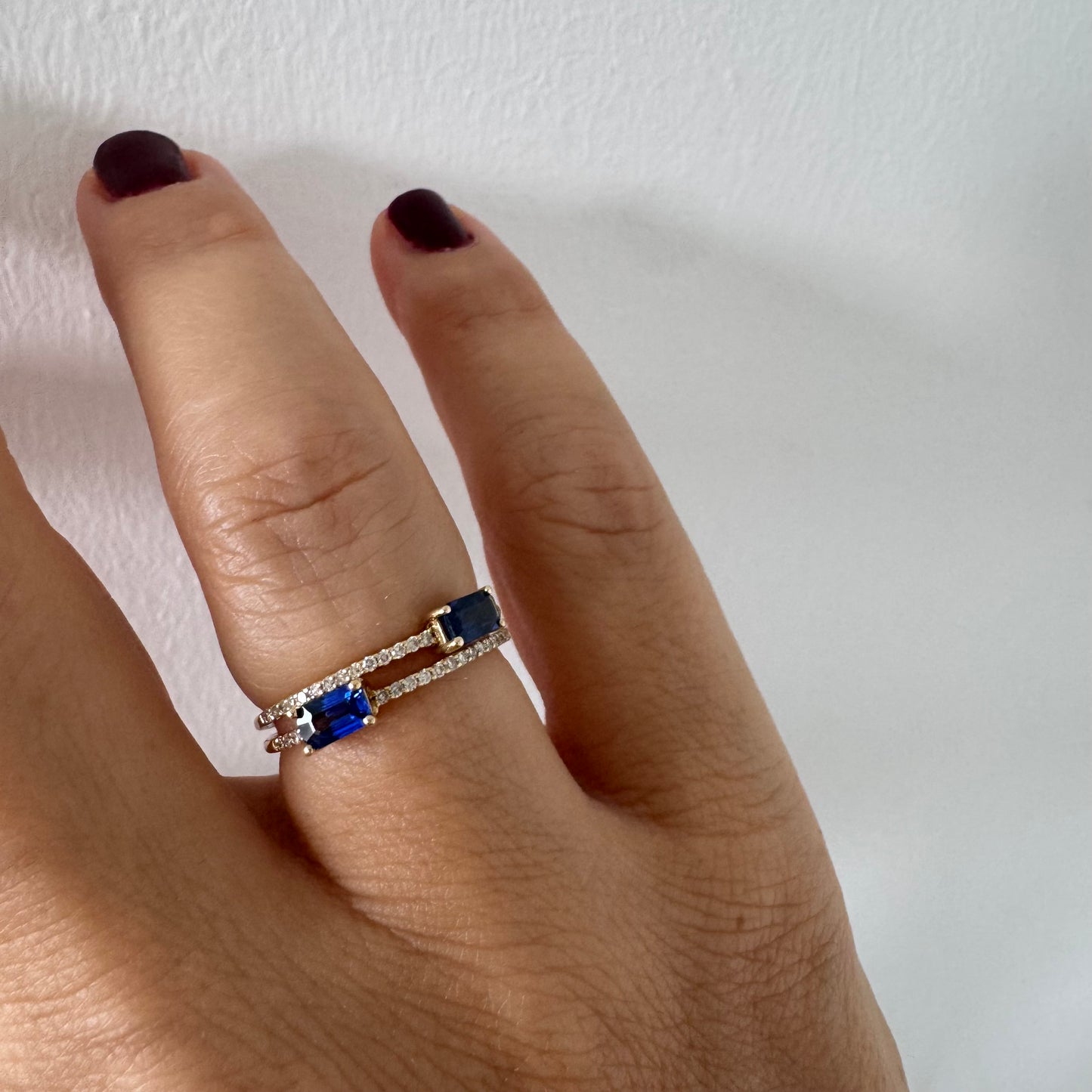 טבעת זהב צהוב 14 קראט בעיצוב פתוח, משובצת שתי אבני ספיר בחיתוך אמרלד ושורות יהלומים עדינים.