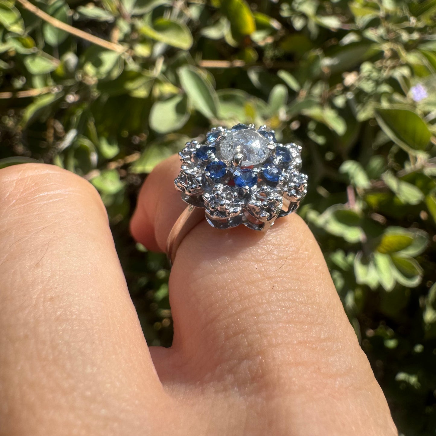 18K gold ring featuring a large round Diamond at the center, surrounded by a floral halo of purple -blue Tanzanite and & Diamonds.