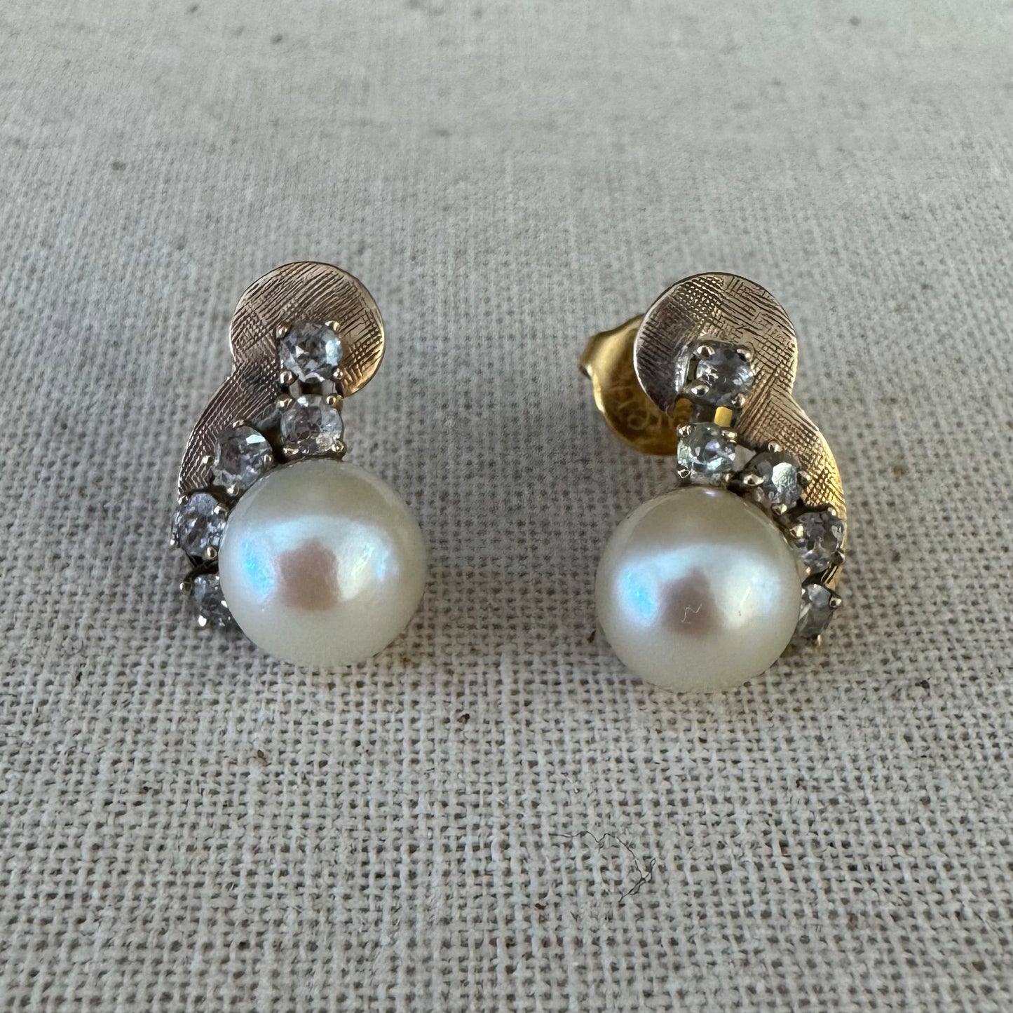 עגילי זהב צהוב 14 קראט, צמודים לאוזן, עשויים זהב בגימור טקסטורלי ומשובצים פנינה עגולה ובשורת יהלומים קטנים בחיתוך עתיק.