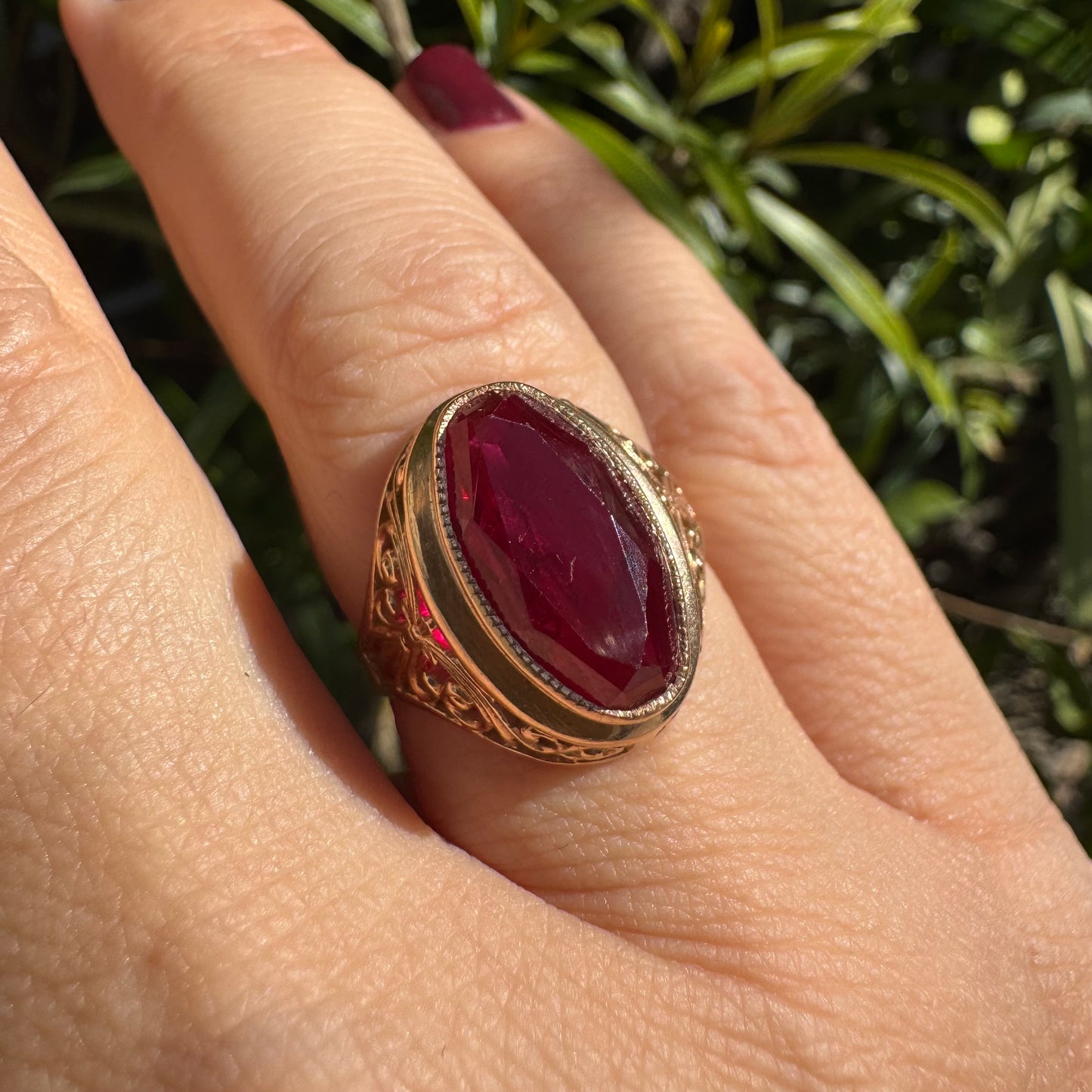 14K gold ring crowned with a vivid oval-cut Ruby, framed in an ornate bezel and accented by intricate filigree details