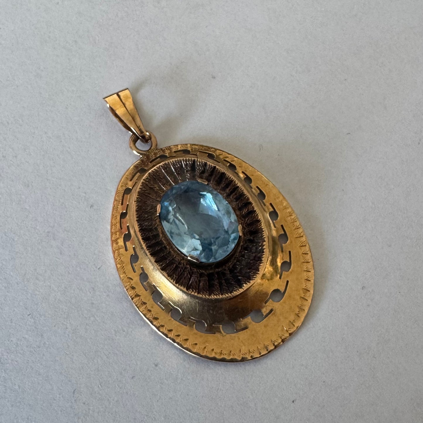תליון מרשים זהב צהוב 14 קראט, בעיצוב אובלי עשיר עם עבודת זהב דקורטיבית ופרטים חרוטים ובמרכז משובצת אבן טופז כחולה גדולה בחיתוך אובלי, שמעניקה לתליון נוכחות וצבע עמוק.