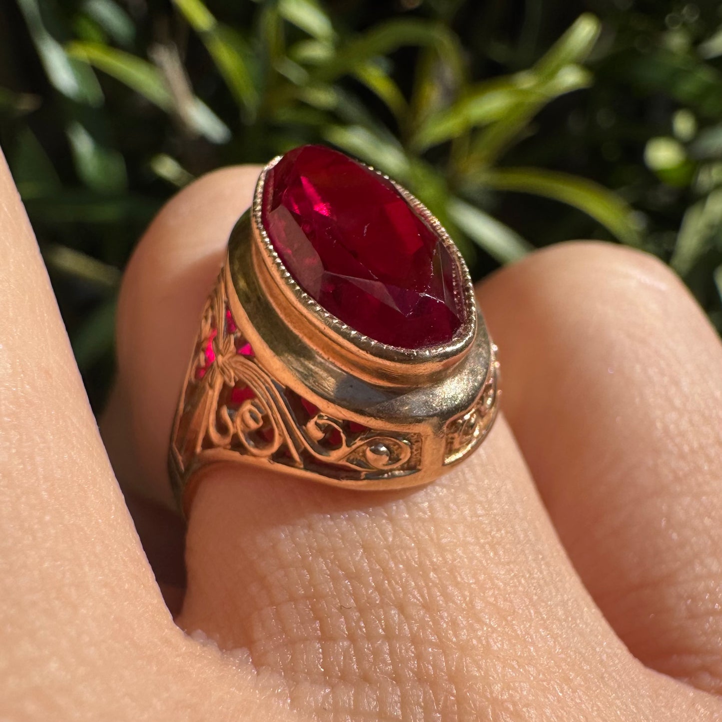 14K gold ring crowned with a vivid oval-cut Ruby, framed in an ornate bezel and accented by intricate filigree details