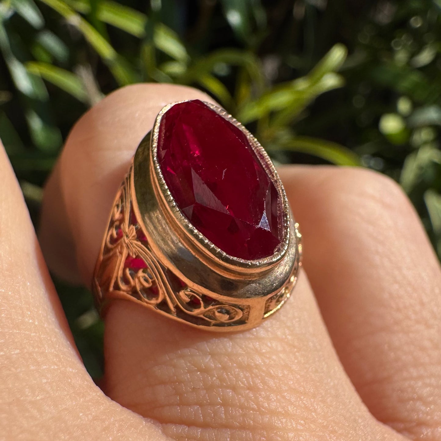 14K gold ring crowned with a vivid oval-cut Ruby, framed in an ornate bezel and accented by intricate filigree details
