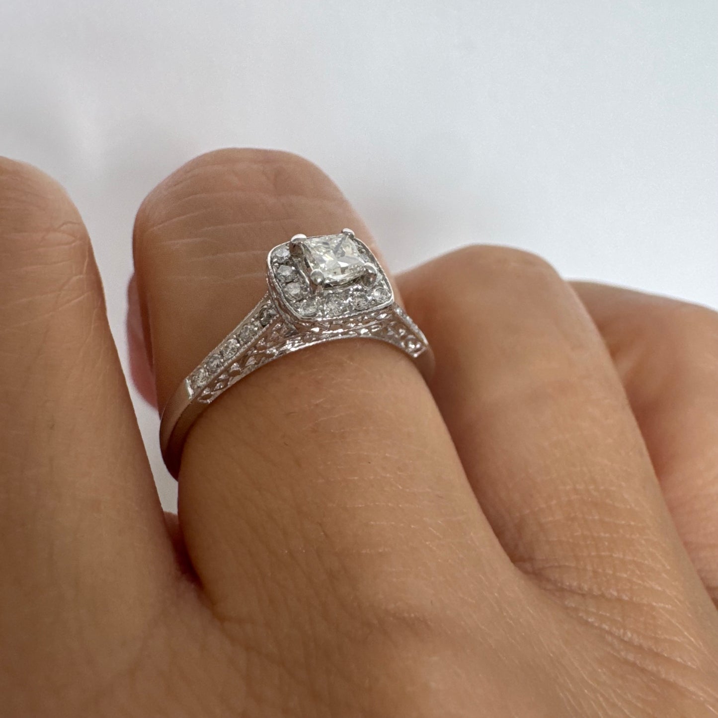 טבעת זהב לבן 14 קראט משובצת יהלום מרכזי בחיתוך פרינסס, מוקף הילת יהלומים קטנים וזרוע משובצת פאווה