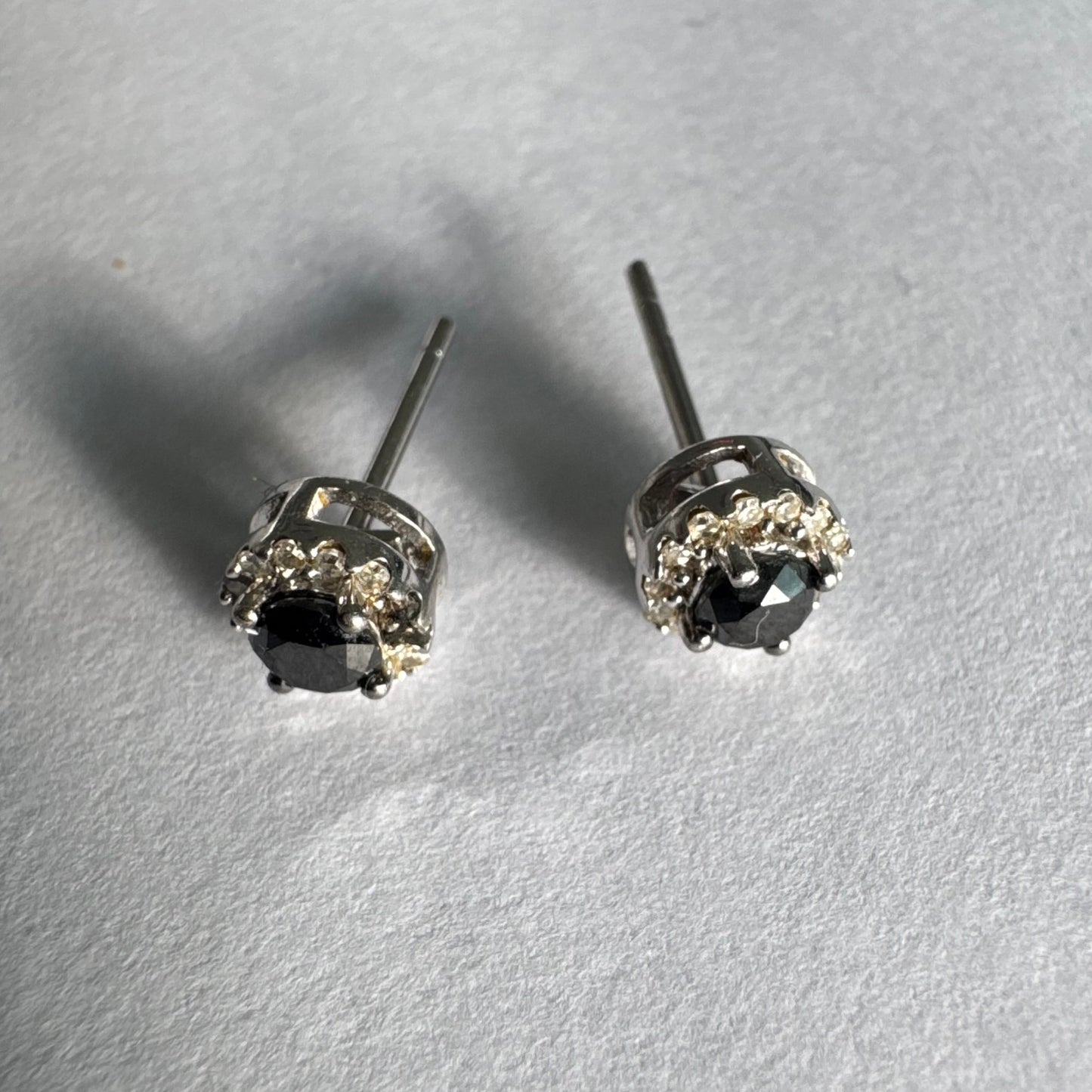 עגילי זהב לבן 10 קראט צמודים לאוזן, משובצים יהלומים שחורים עגולים במרכז ומסביבם הילה של יהלומים לבנים מנצנצים.