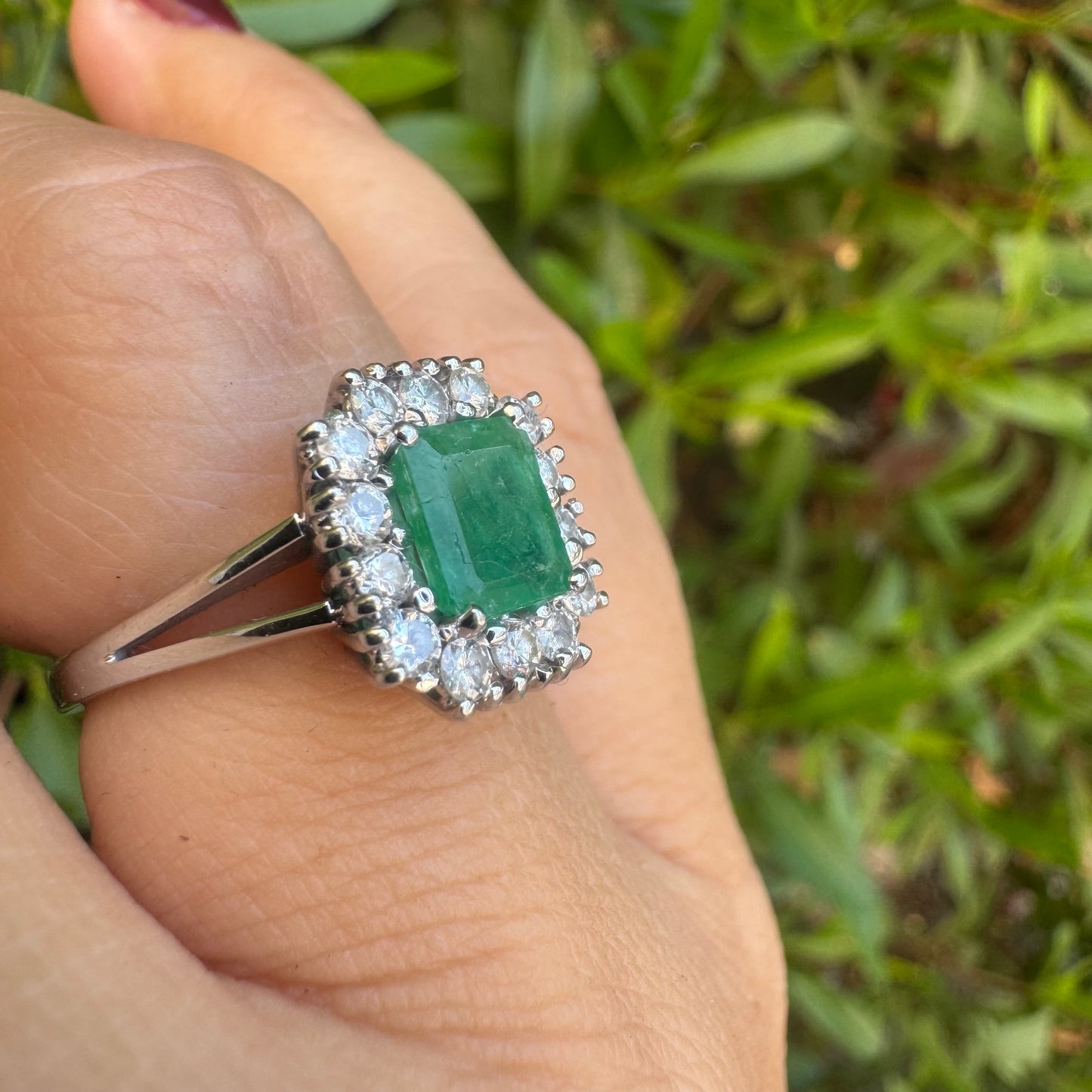 18K gold ring set with a green Emerald at the center, surrounded by a halo of sparkling round Diamonds.