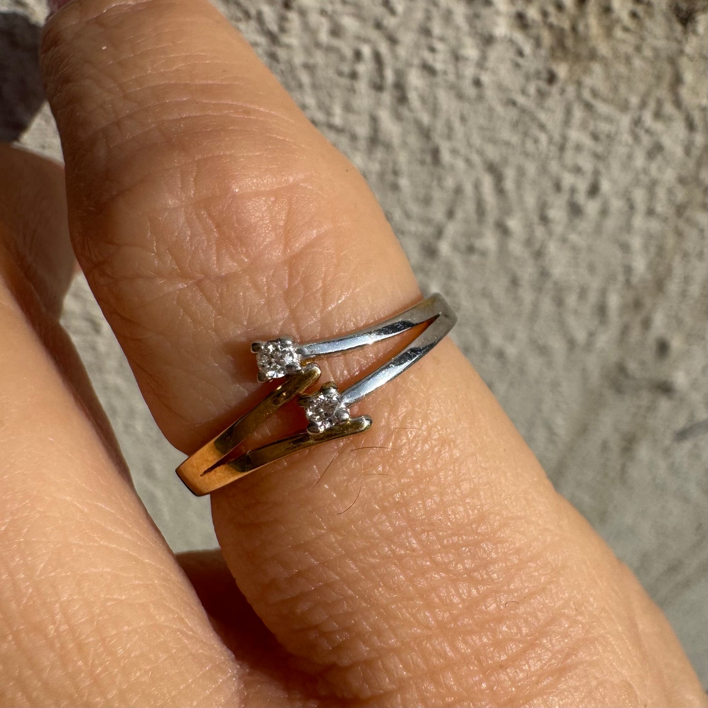 טבעת זהב 14 קראט, עם זרועות מצטלבות בזהב צהוב וזהב לבן, שכל אחת מהן משובצת יהלום קטן ונוצץ.