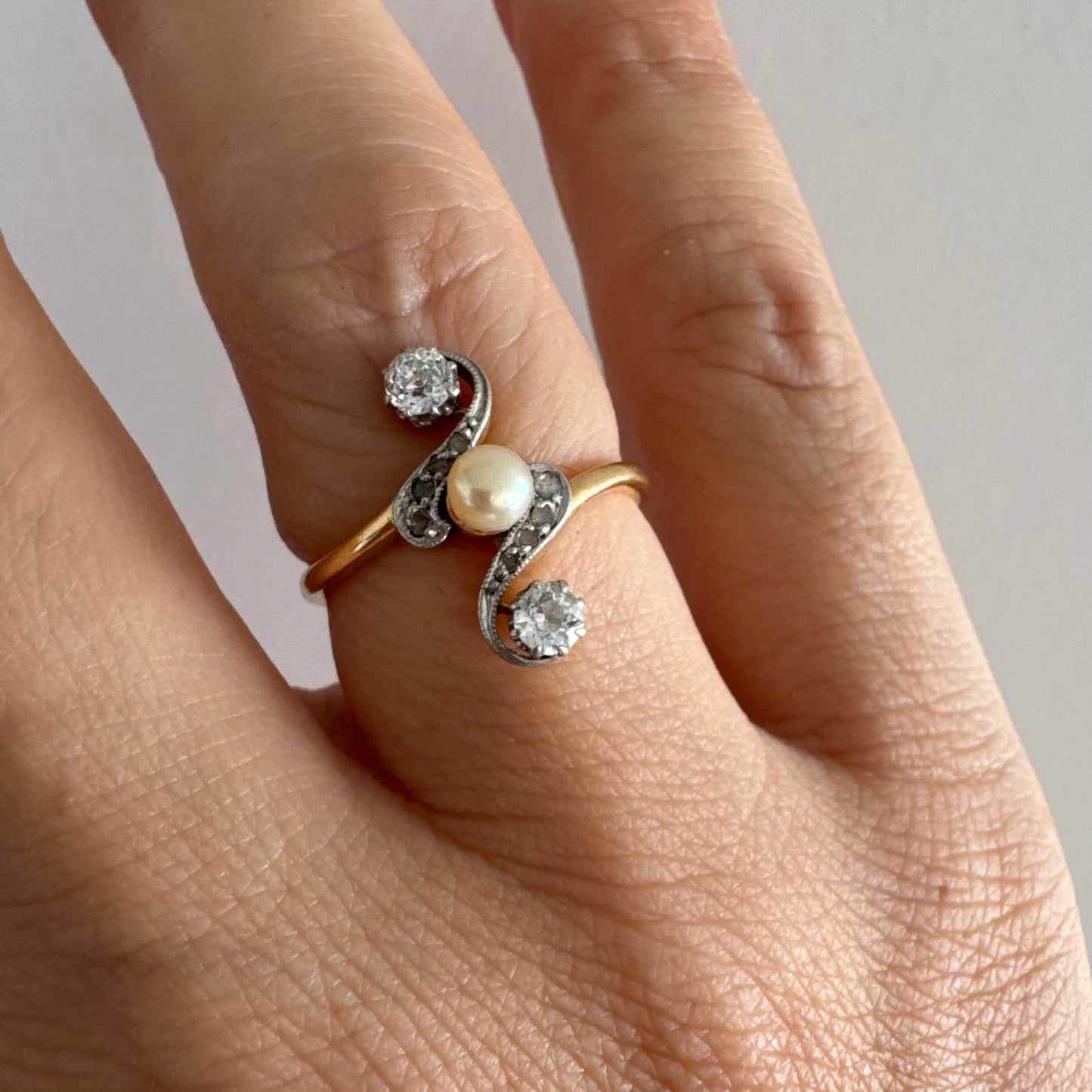 טבעת זהב 18 קראט בעיצוב וינטג׳ קלאסי, משובצת בשני יהלומים בחיתוך עתיק ובפנינה טבעית במרכז.