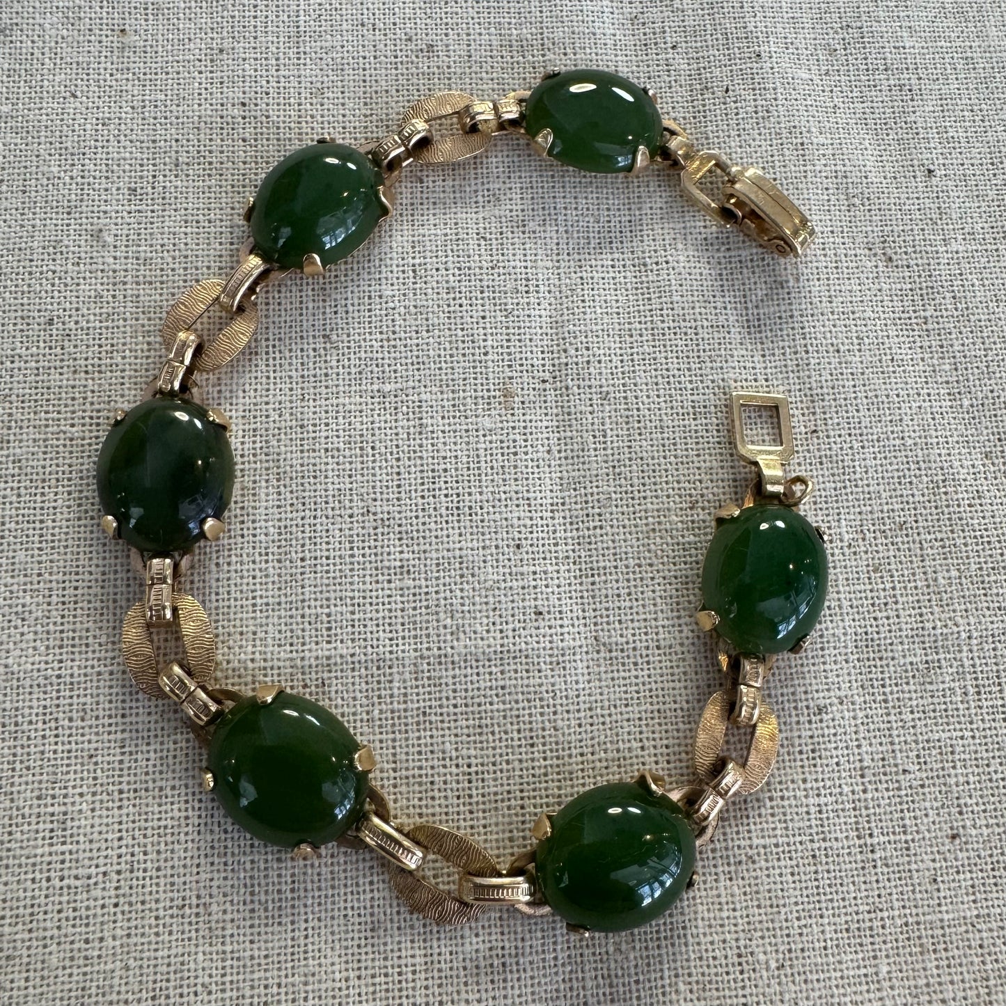 צמיד זהב צהוב 14 קראט משובץ באבני ג’ייד ירוקות בחיתוך קבושון (cabochon) בעיצוב אליפטי, המחוברות ביניהן בחוליות זהב עם טקסטורה מעניינת.