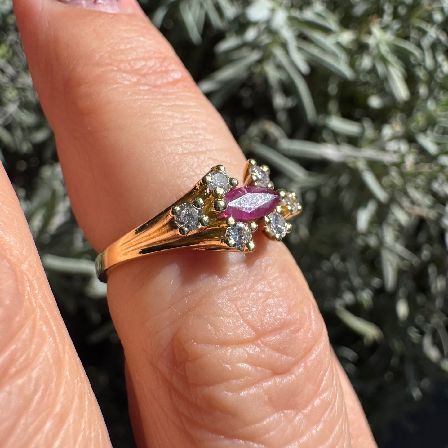 טבעת זהב צהוב 18 קראט משובצת אבן רובי בחיתוך מרקיזה בגוון מוקפת יהלומים בחיתוך עגול משני הצדדים.