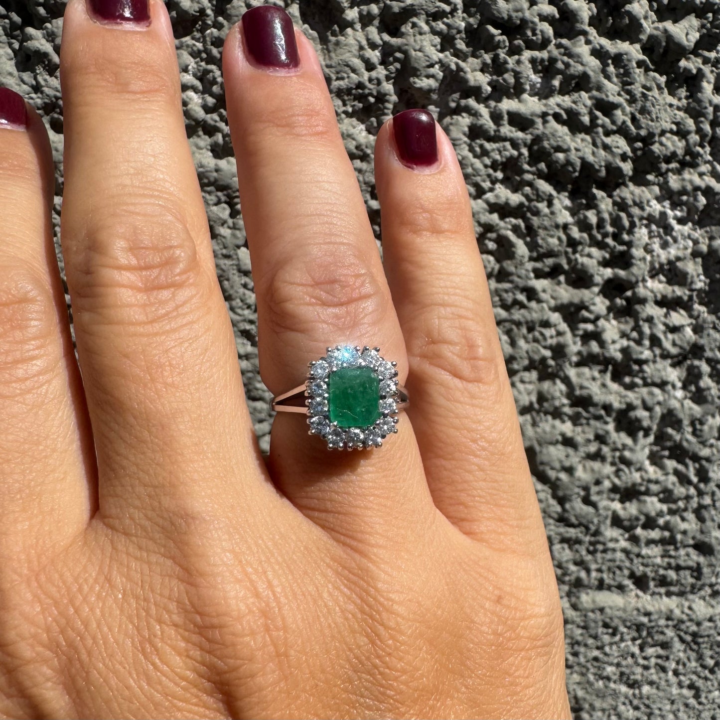 18K gold ring set with a green Emerald at the center, surrounded by a halo of sparkling round Diamonds.