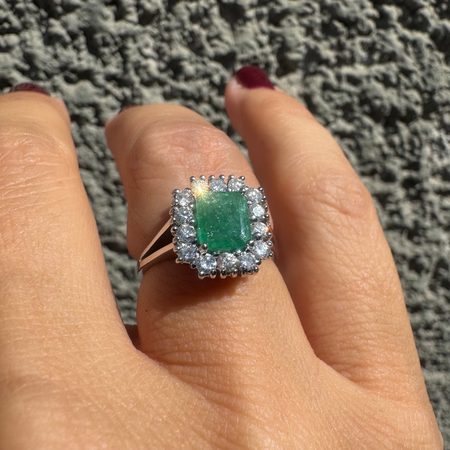 18K gold ring set with a green Emerald at the center, surrounded by a halo of sparkling round Diamonds.
