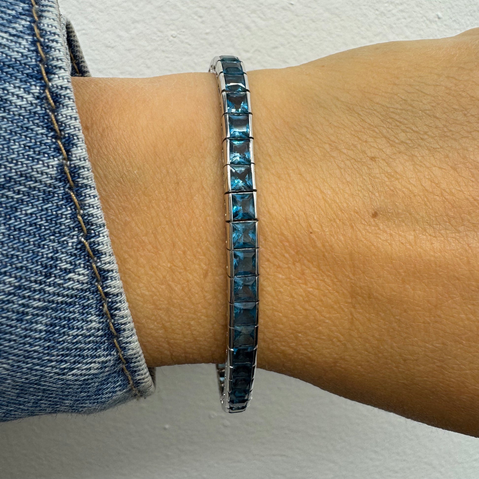 צמיד זהב לבן 18 קראט של המותג ה.שטרן משובץ אבני טופז כחולה&nbsp;בשיבוץ ערוץ חלק וקלאסי – פריט נצחי עם טאץ’ מודרני