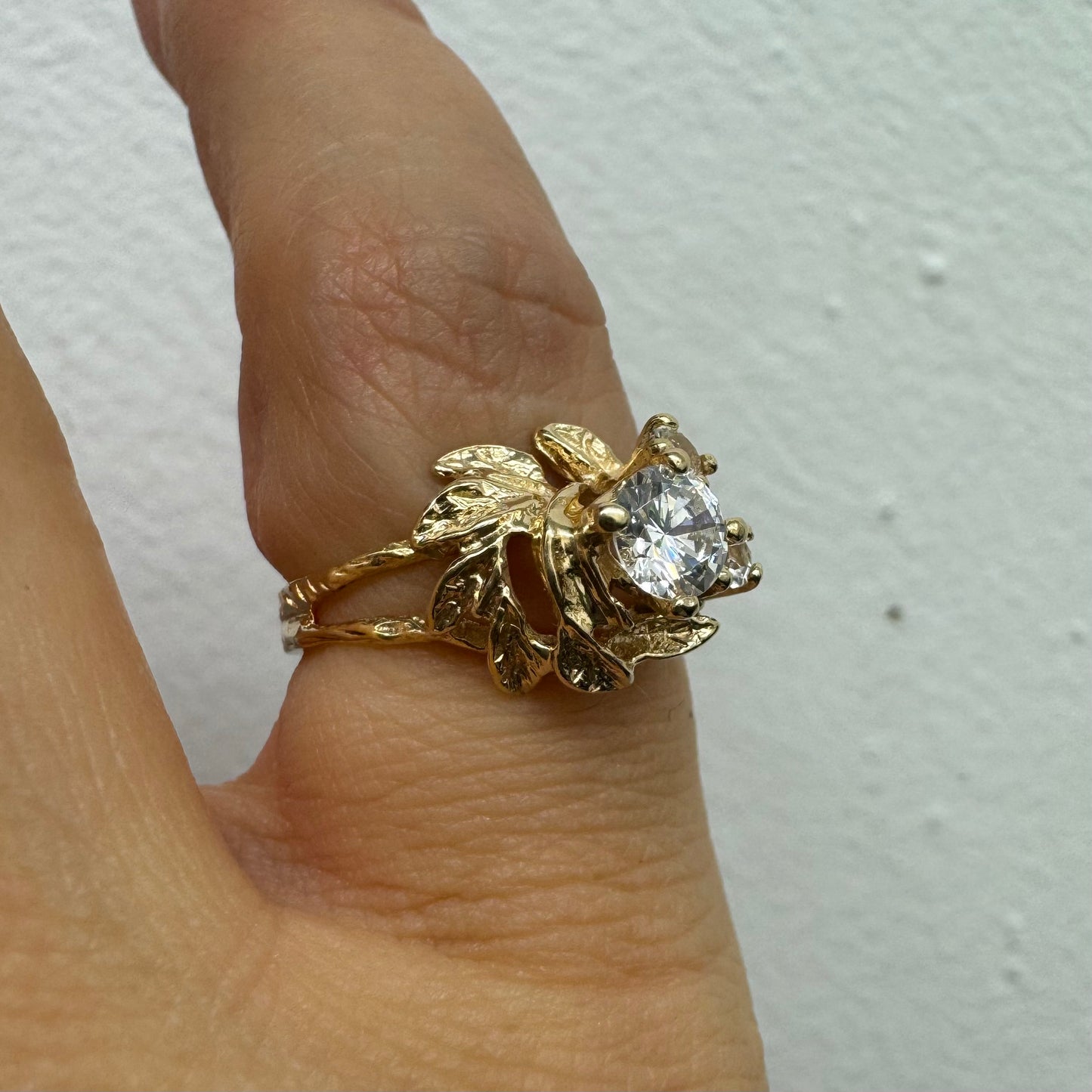 טבעת זהב צהוב 14 קראט בעלת עיצוב אורגני עשיר עם עלים מגולפים סביב שלוש אבנים שקופות נוצצות. (לא יהלומים)